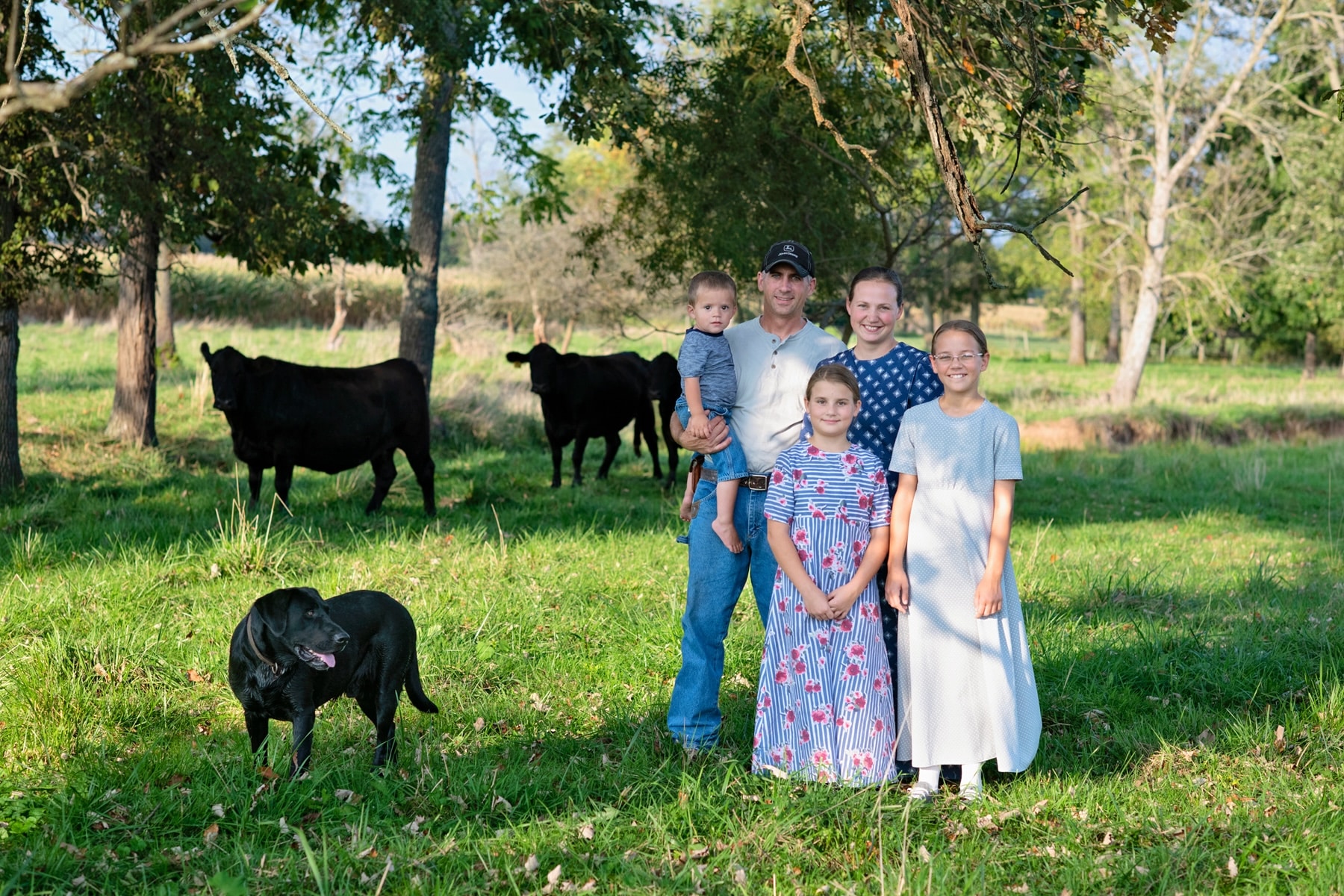 The family of Pond Bank Farm poses with their dog in front of steers.