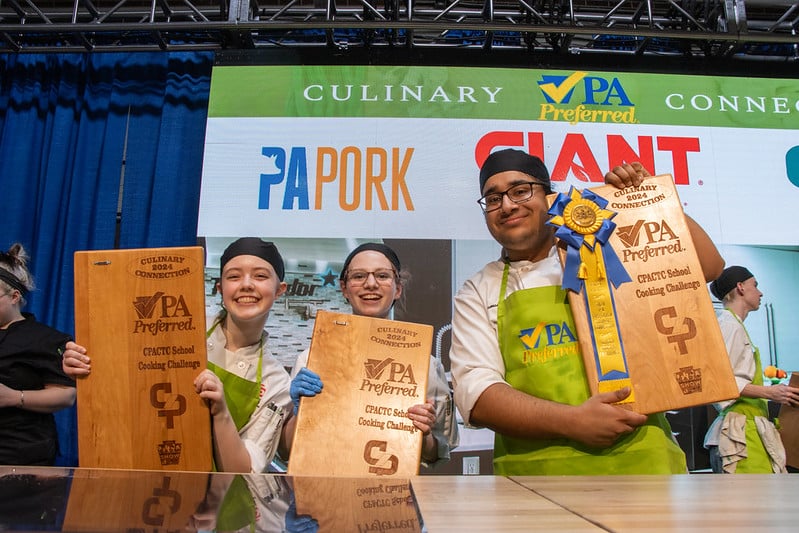 Team one student chefs, Grace, Leah, and Roman hold up their first place awards from the Culinary Connections School Cooking Challenge Friday evening on the Culinary Connections Stage.